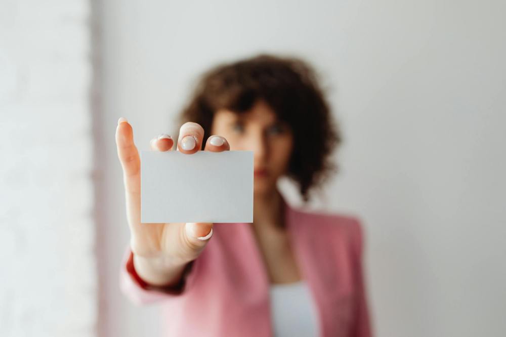 woman in pink long sleeve shirt holding white card